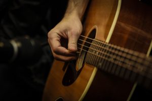 Image showing a guitarist's right hand holding a plectrum and picking individual strings in guitar lessons